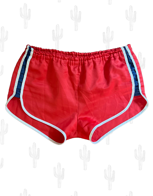 Front image of red gym shorts with navy stripes on light background.