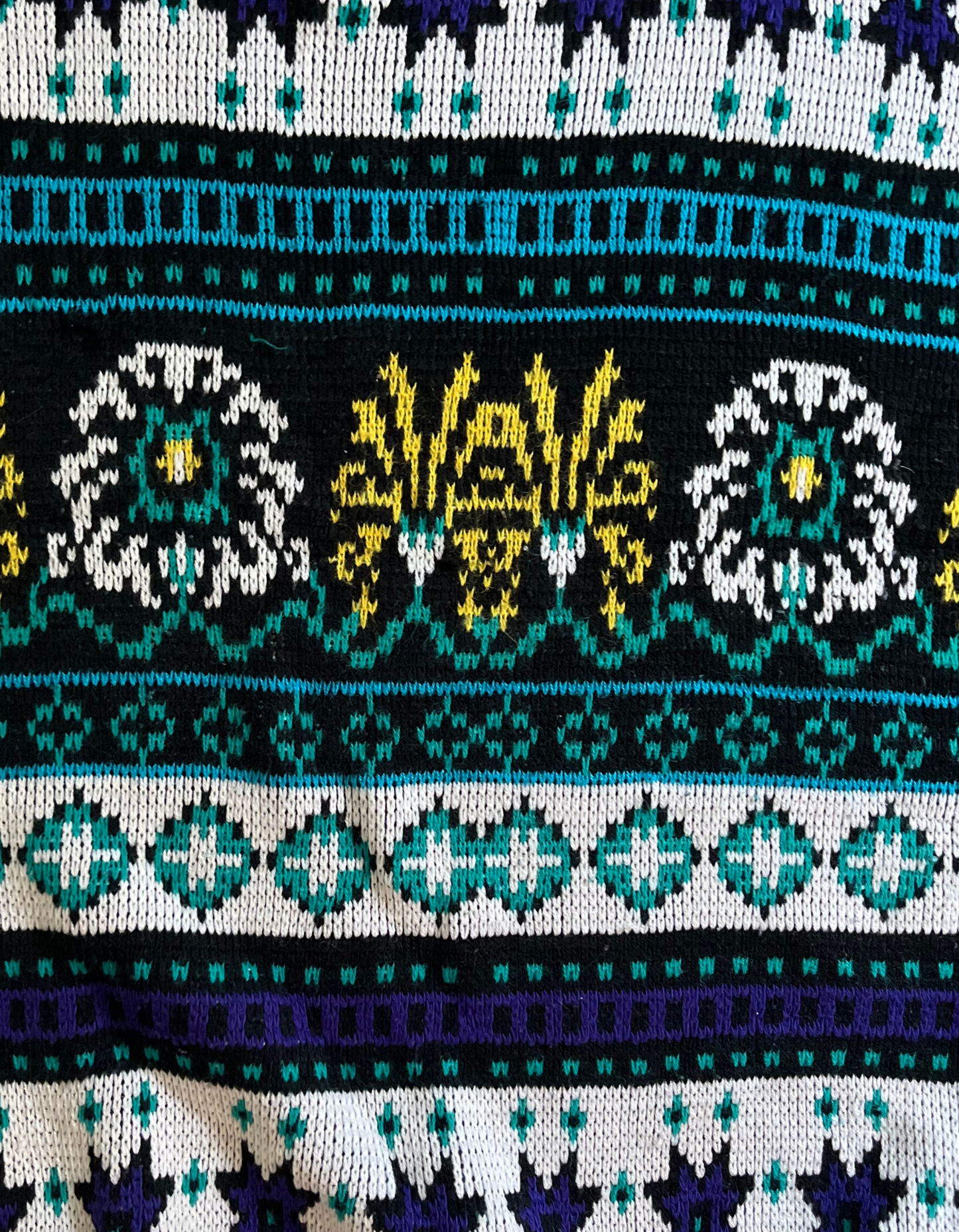 Close up image of purple, white, teal, black and yellow sweater on white background.