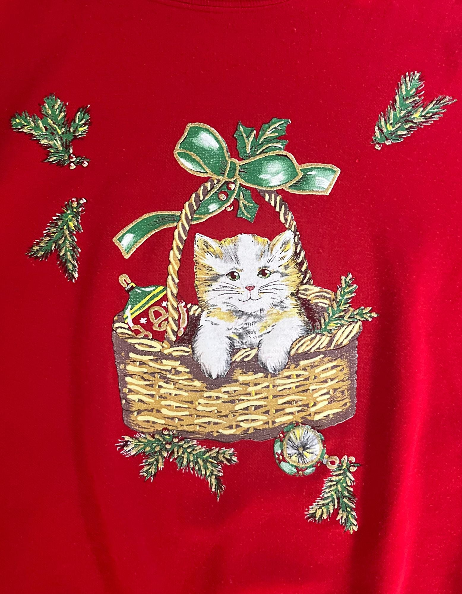 Close up image of red christmas sweatshirt featuring kitty cat in basket on white background.