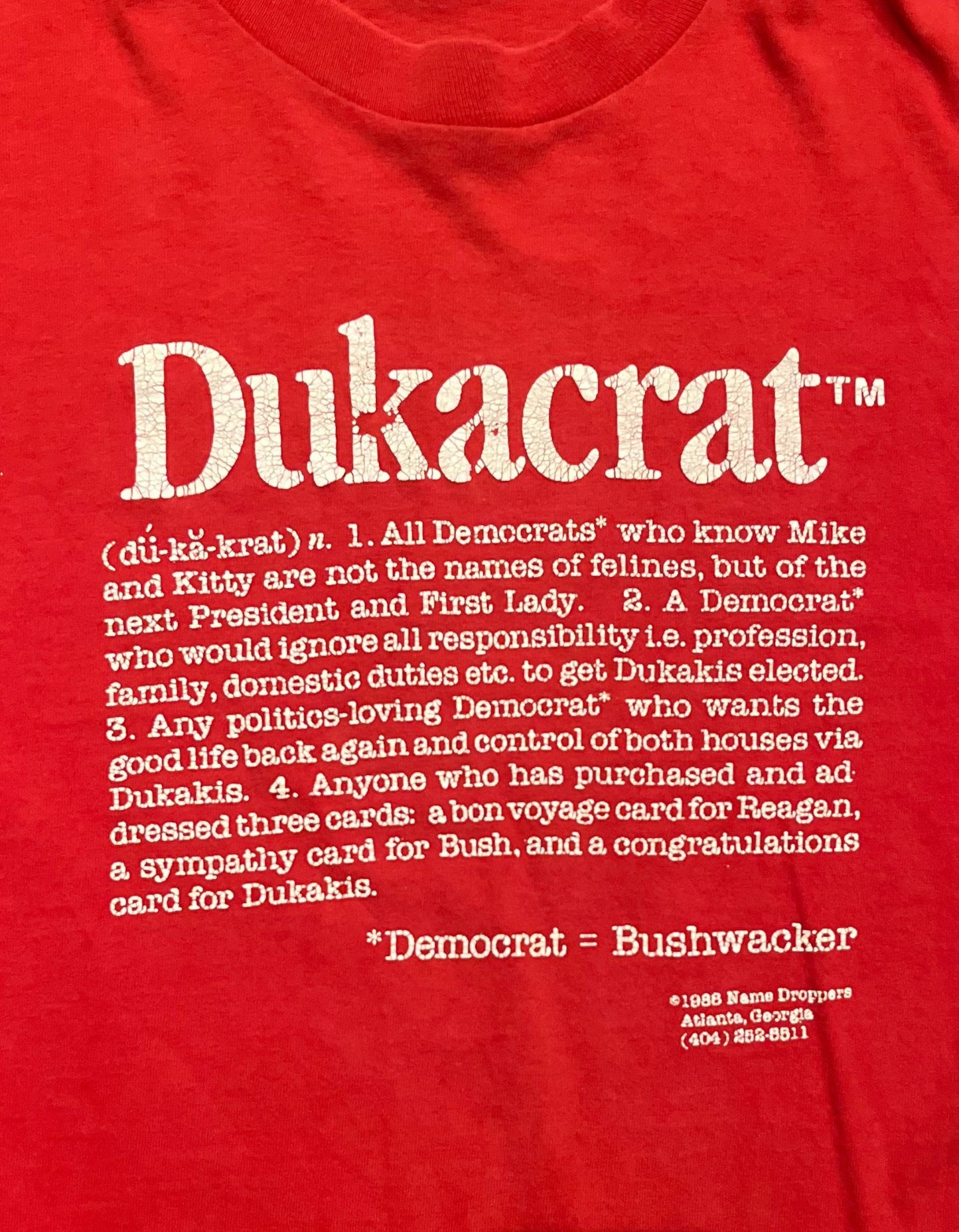 Front of red 1988 Dukacrat tshirt with white text on white background close up on text.